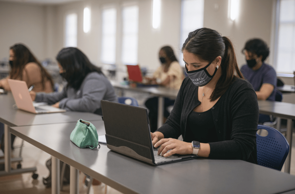 student looking at laptop in the classroom with central Piedmont face mask on