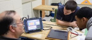 Two students and instructor using technology to examine a weld with a screen on a table