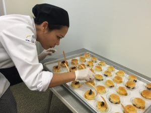 Chef in chef coat preparing many small individual desserts on table