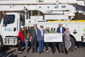 Group of people in hard hats standing in front of a Duke Energy truck with a bucket arm, holding a large check.