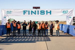 a group of participants stand under the finish line banner at the Charlotte CLT Airport Runway 5K event