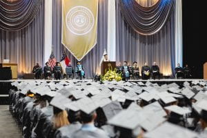 Graduates wearing gray cap and gown listen to the student commencement speaker