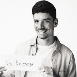 Jorge is smiling and  holding a sign that reads "new beginnings"