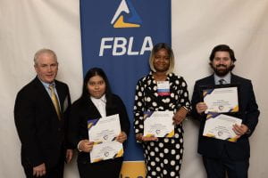 Students stand holding certificates with their advisor in front of an FBLA banner.