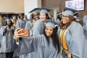 A group of graduates wearing caps and gowns smile during a selfie