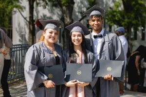 3 graduates smile while holding their diploma folders.