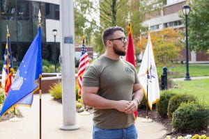 Student Veteran stands by the flagpole and military